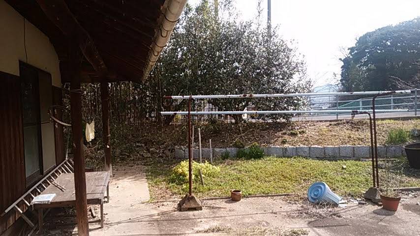 Under the eaves of the house, drying poles standing over an overgrown garden