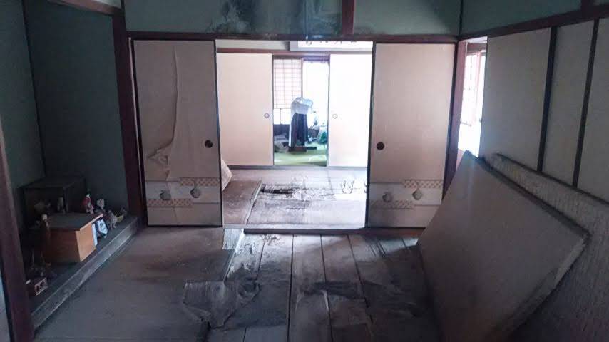 A tatami room before restoration, floorboards collapsed and a mat propped against the wall