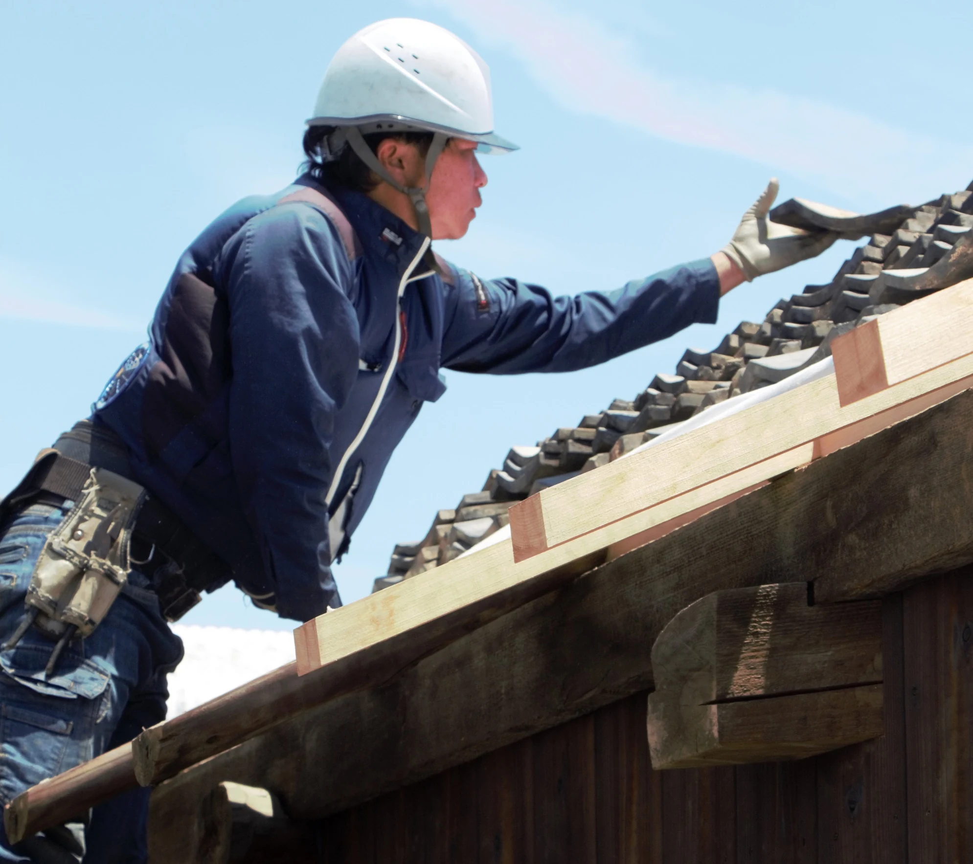 A roofer setting clay tiles along the ridge of the house against a clear sky