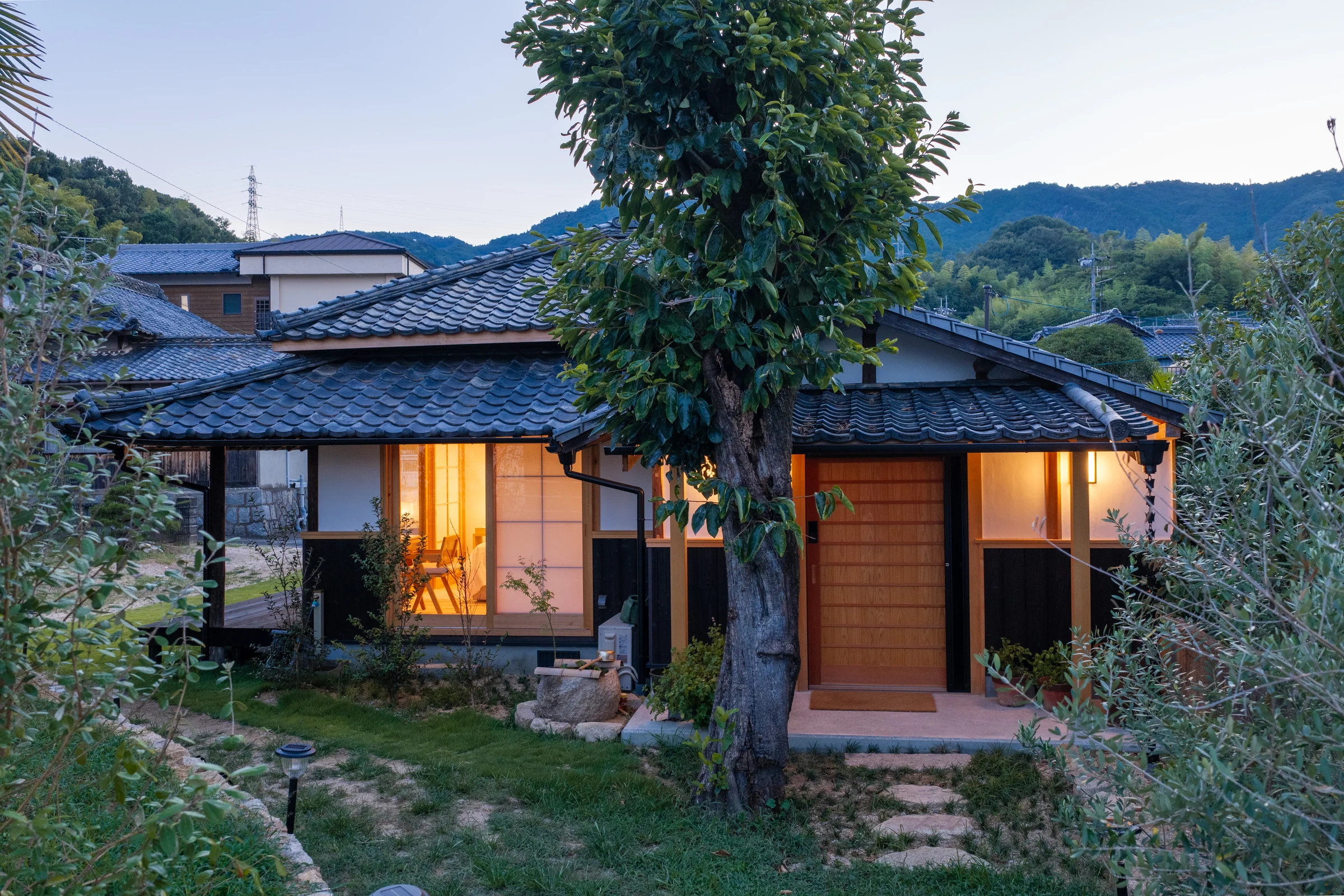 The Tea House at dusk in island mist, lamplight glowing behind its shoji screens